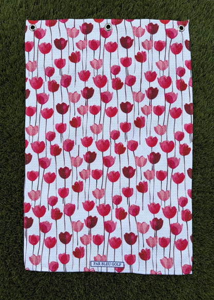 Red tulip golf towel laid flat on green grass, showcasing feminine floral design and soft microfiber material