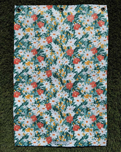 Women’s golf towel laid flat on grass, showcasing teal and orange daisy print and lightweight microfiber fabric