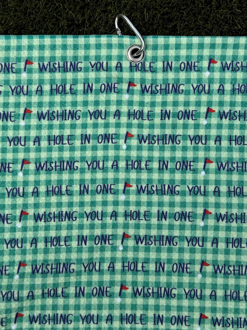 Golf towel in green color with metal carabiner, featuring repeated motivational phrase “Wishing You a Hole in One”