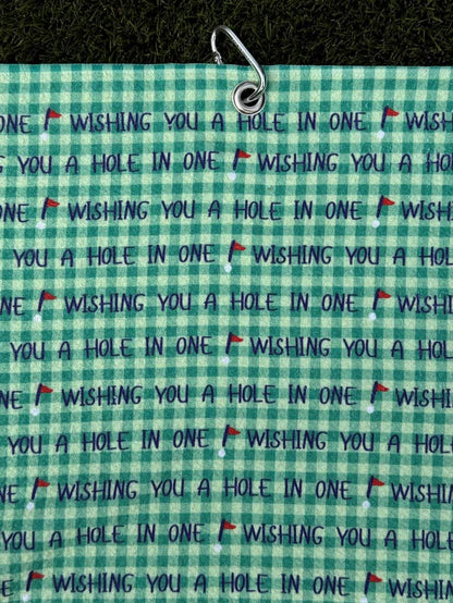 Golf towel in green color with metal carabiner, featuring repeated motivational phrase “Wishing You a Hole in One”